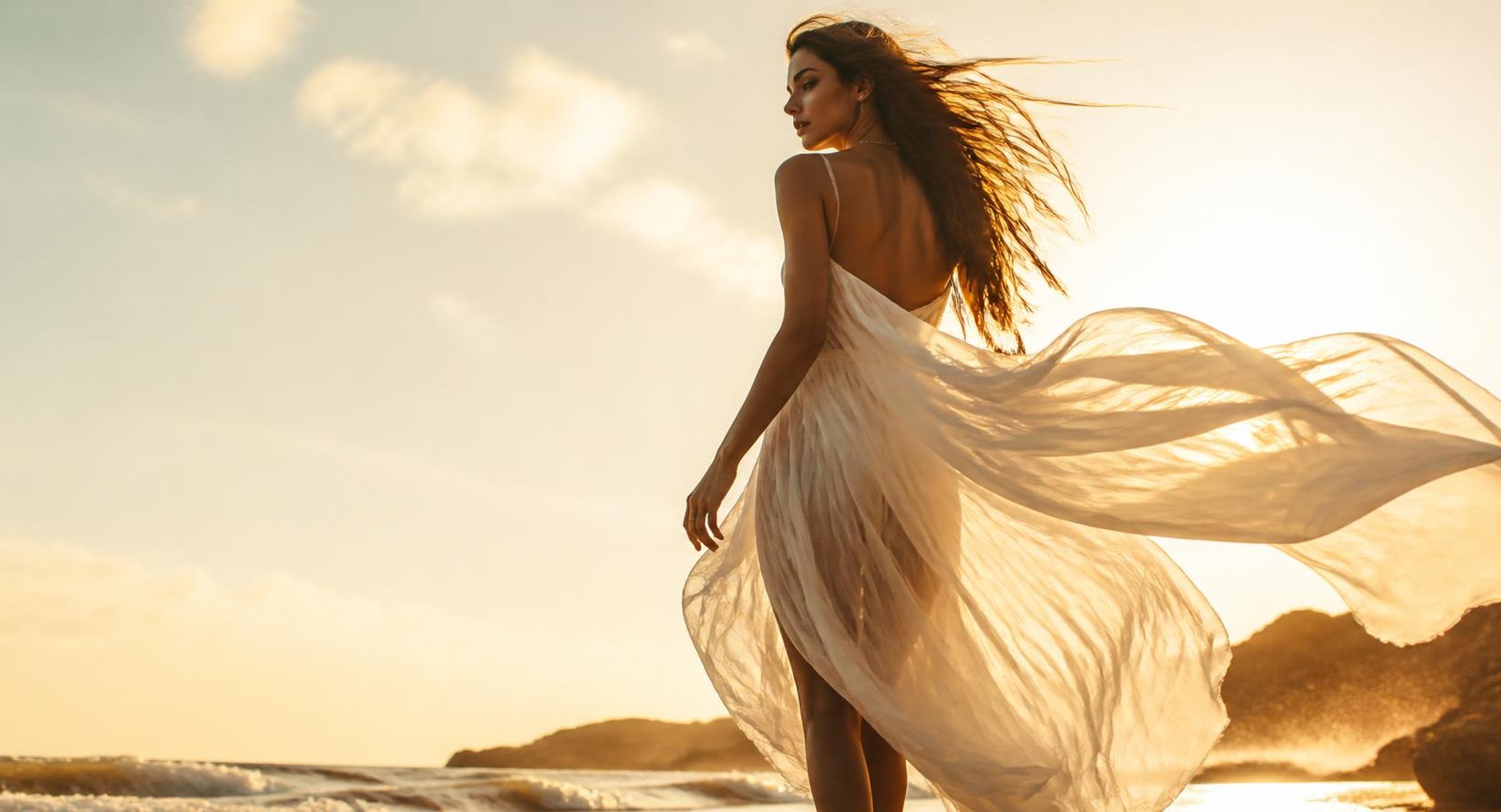 Woman in a flowing white chiffon dress on the shoreline at golden hour