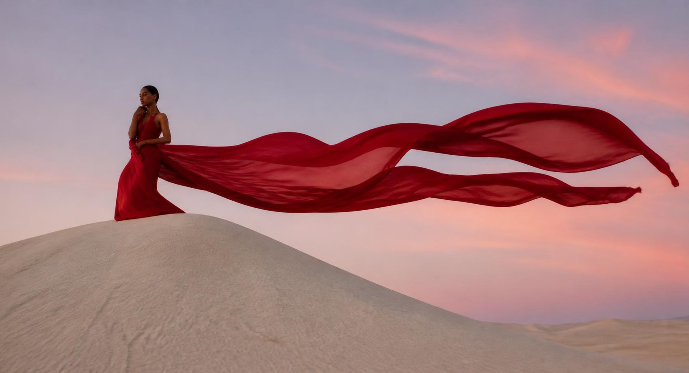 Model in a crimson silk gown billowing on a sand dune at dawn