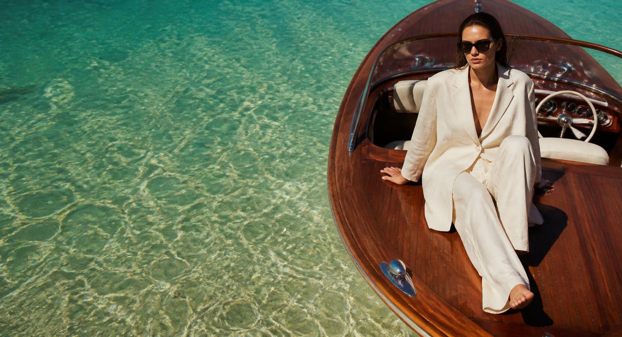 Model in an ivory linen suit on a vintage boat over turquoise water